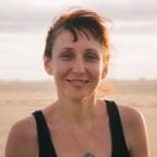 Photo of Jennie F, a with woman looking to the camera smiling and in the backwround the beach.