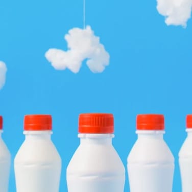 This is a gallery image of a milk bottles with red bottle top with an blue ski background.