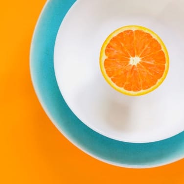 This is a gallery image of an orange in a white plate with a green border, the background is orange.